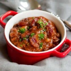 Vegetarian chili in a small red crock bowl, on a gray napkin.