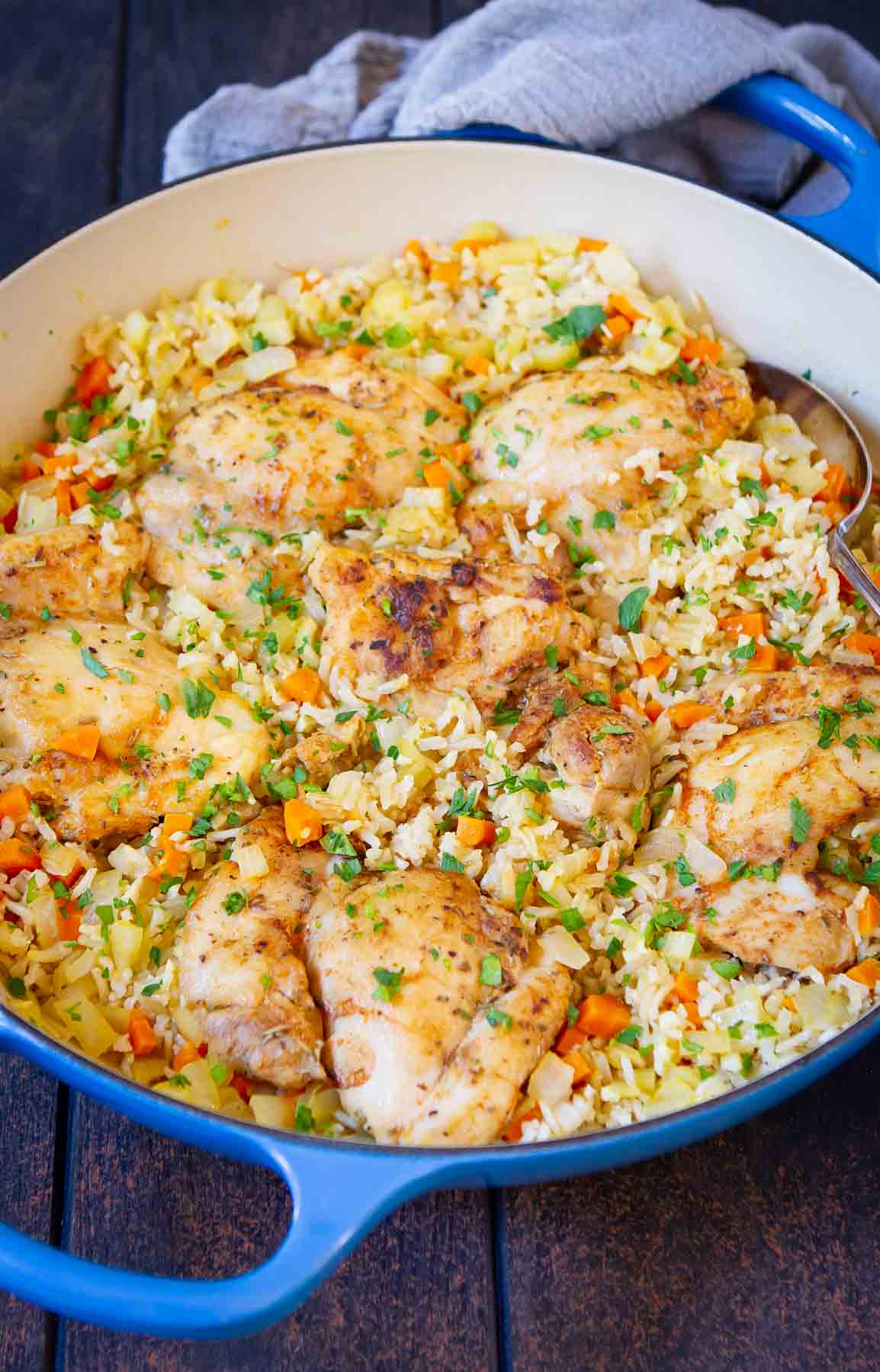 Cooked chicken and rice with spices and vegetables in a blue skillet.