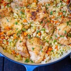 Cooked chicken and rice with spices and vegetables in a blue skillet.