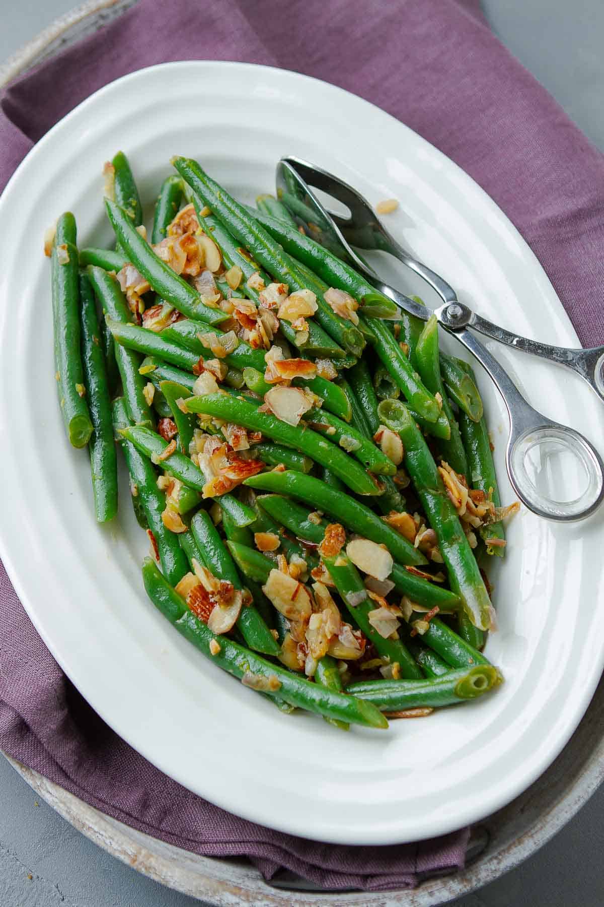 Cooked green beans with almonds and shallots on a white plate.