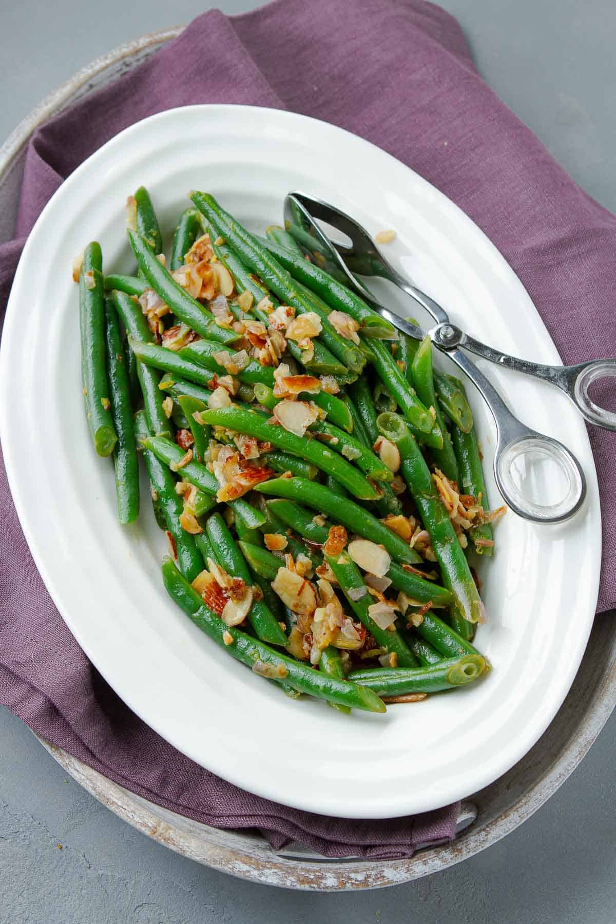 String beans with almonds on a white plate, with a purple napkin underneath.