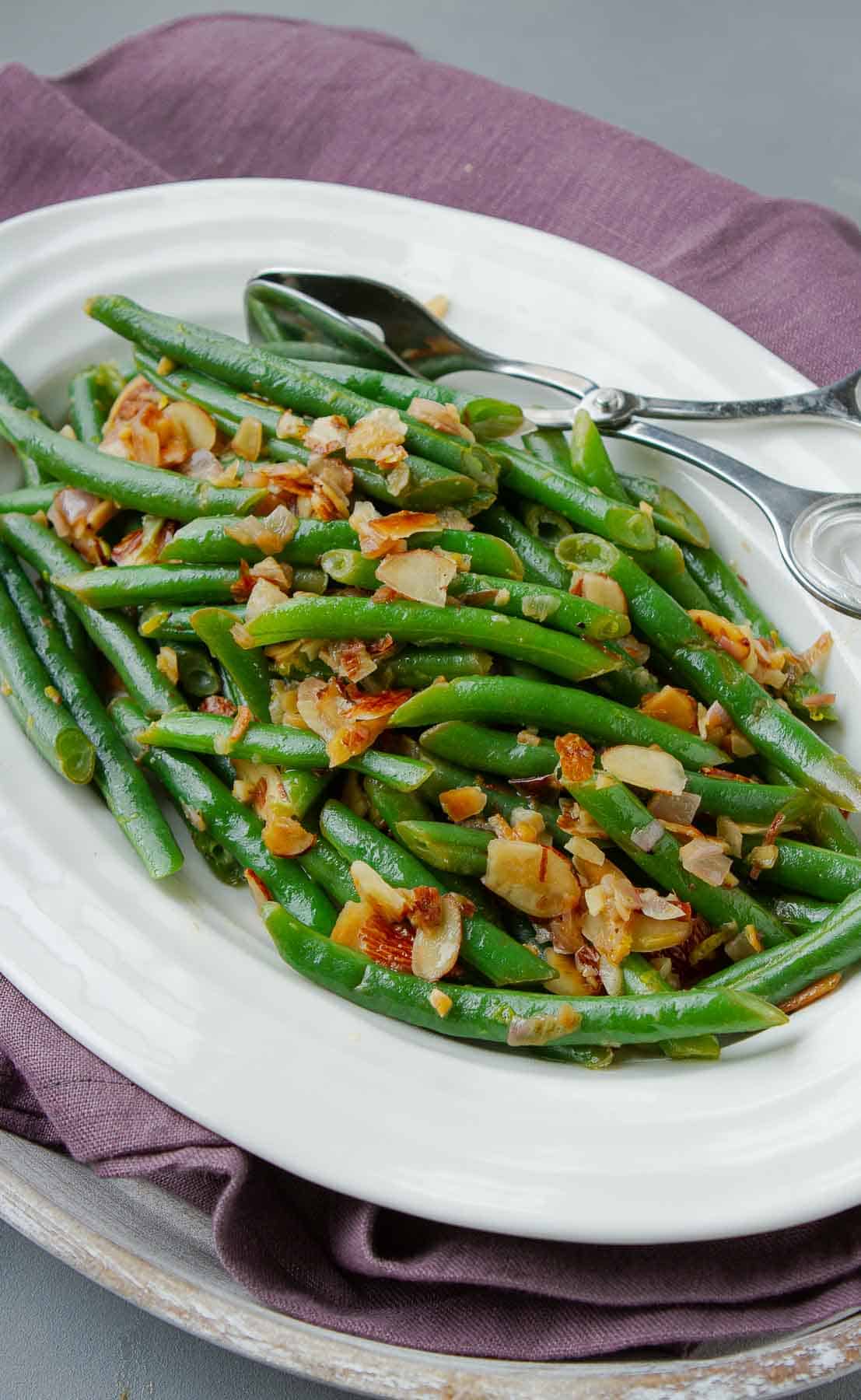 Cooked green beans on a white plate with toasted almonds.