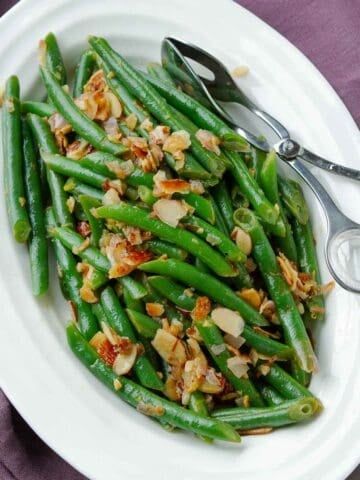 Sautéed green beans with almonds and shallots on a white plate.
