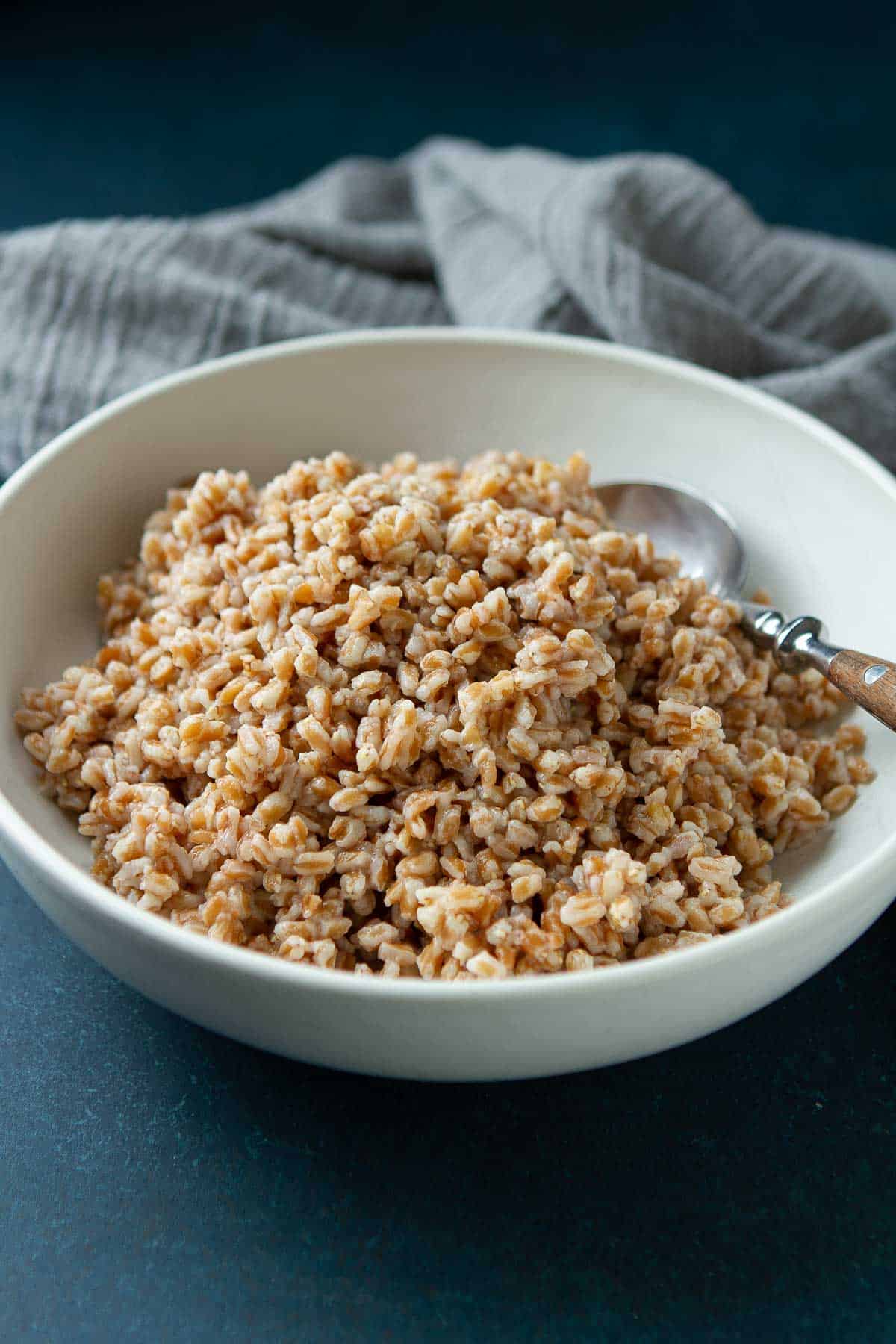 Cooked Instant Pot farro in a white bowl, with gray napkin on the side.