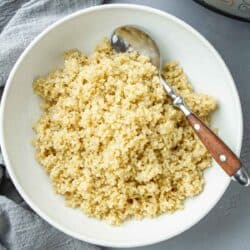 Cooked quinoa in a white bowl with a spoon.
