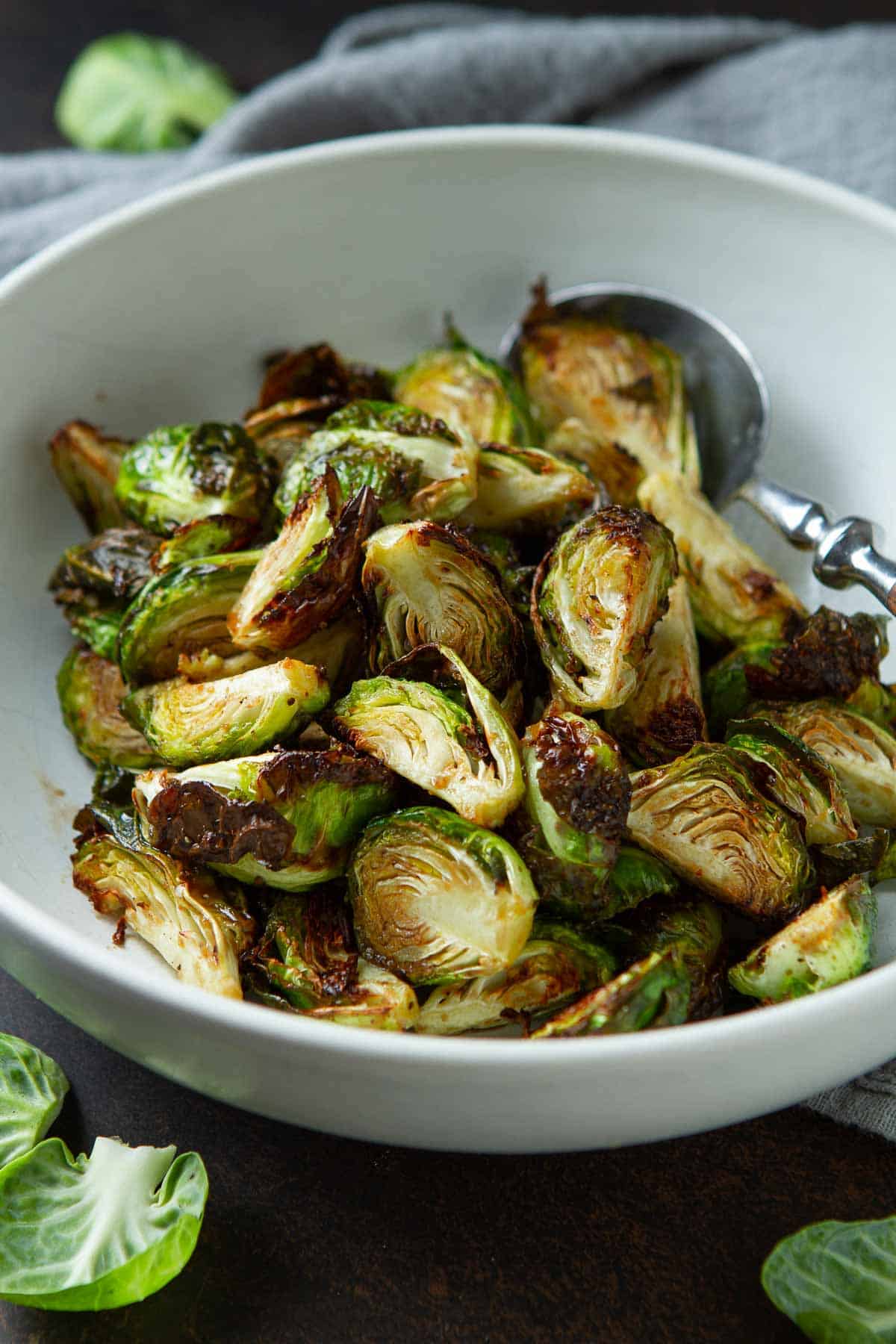 Golden brown Brussels sprouts in a white bowl with a spoon.