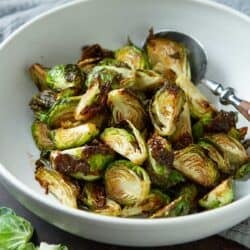 Cooked Brussels sprouts in a white bowl, with a wooden-handled spoon.