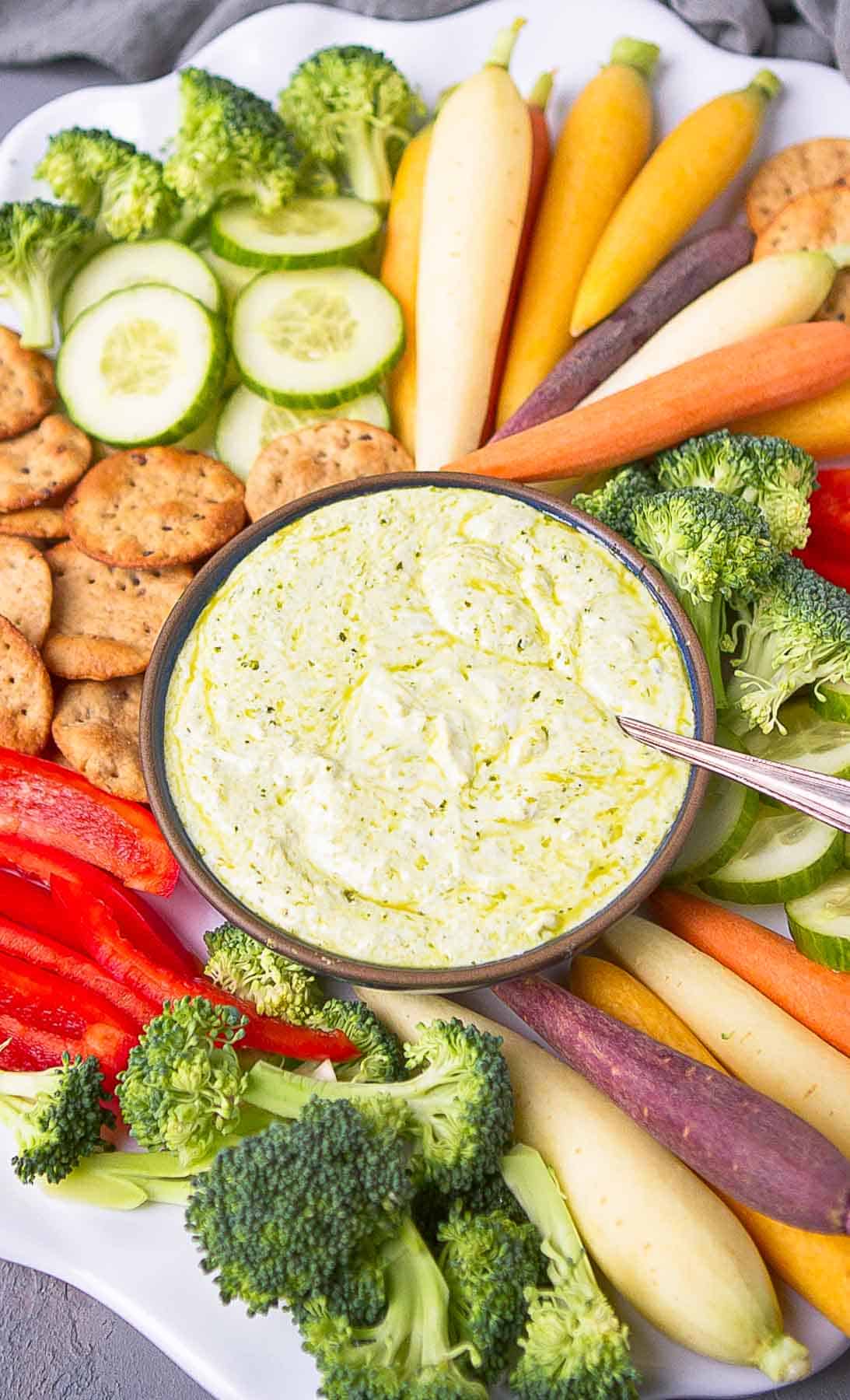 Yogurt dip with pesto in a bowl, with vegetables on a platter.