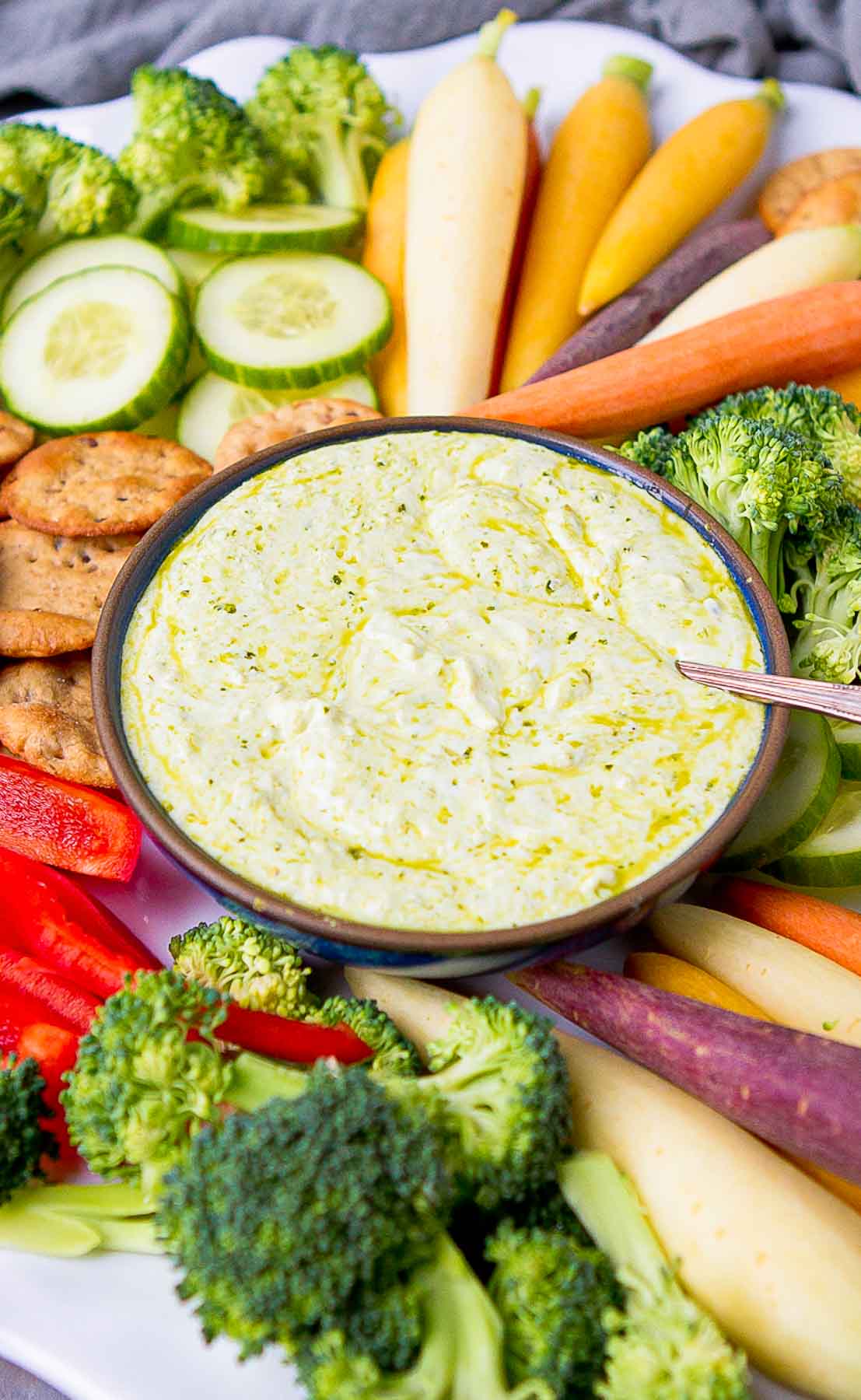 Pesto dip in a bowl, surrounded by raw vegetables and crackers.
