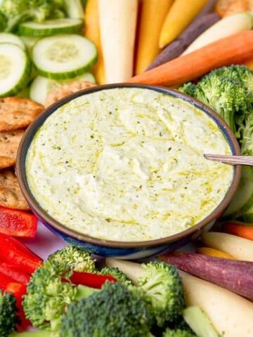 Pesto dip in a bowl, surrounded by raw vegetables and crackers.
