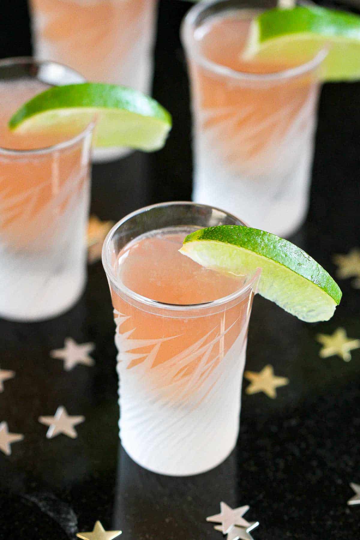 Cut glass shot glasses filled with vodka cranberry kamikaze shots, with lime wedges.