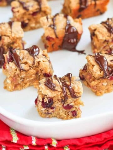 Cranberry oatmeal bars drizzled with chocolate on a white plate and red towel.