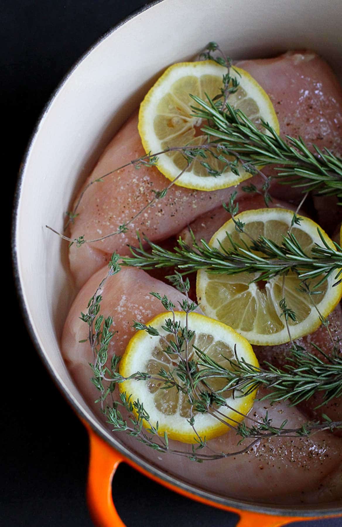 Raw chicken, sprigs of lemon and rosemary in a large pot.