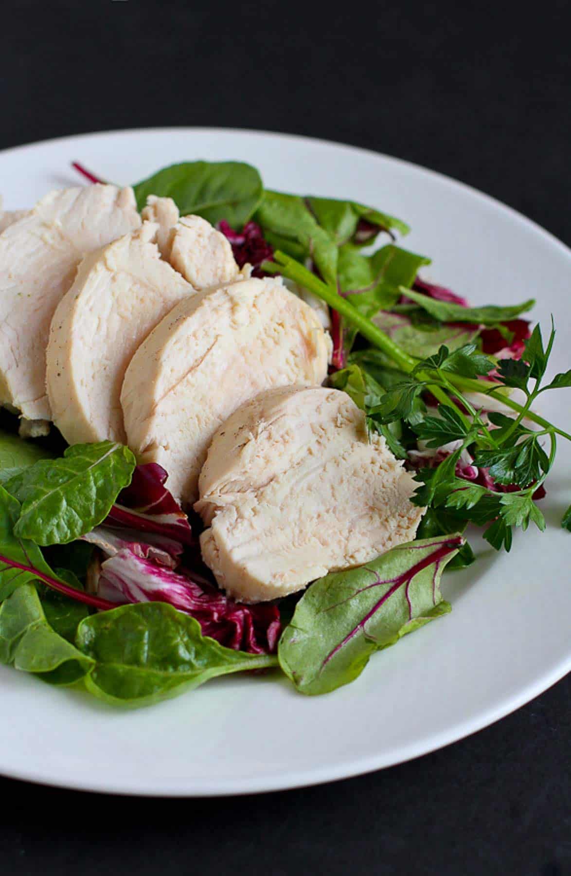 Sliced chicken breast and mixed greens on a white plate.