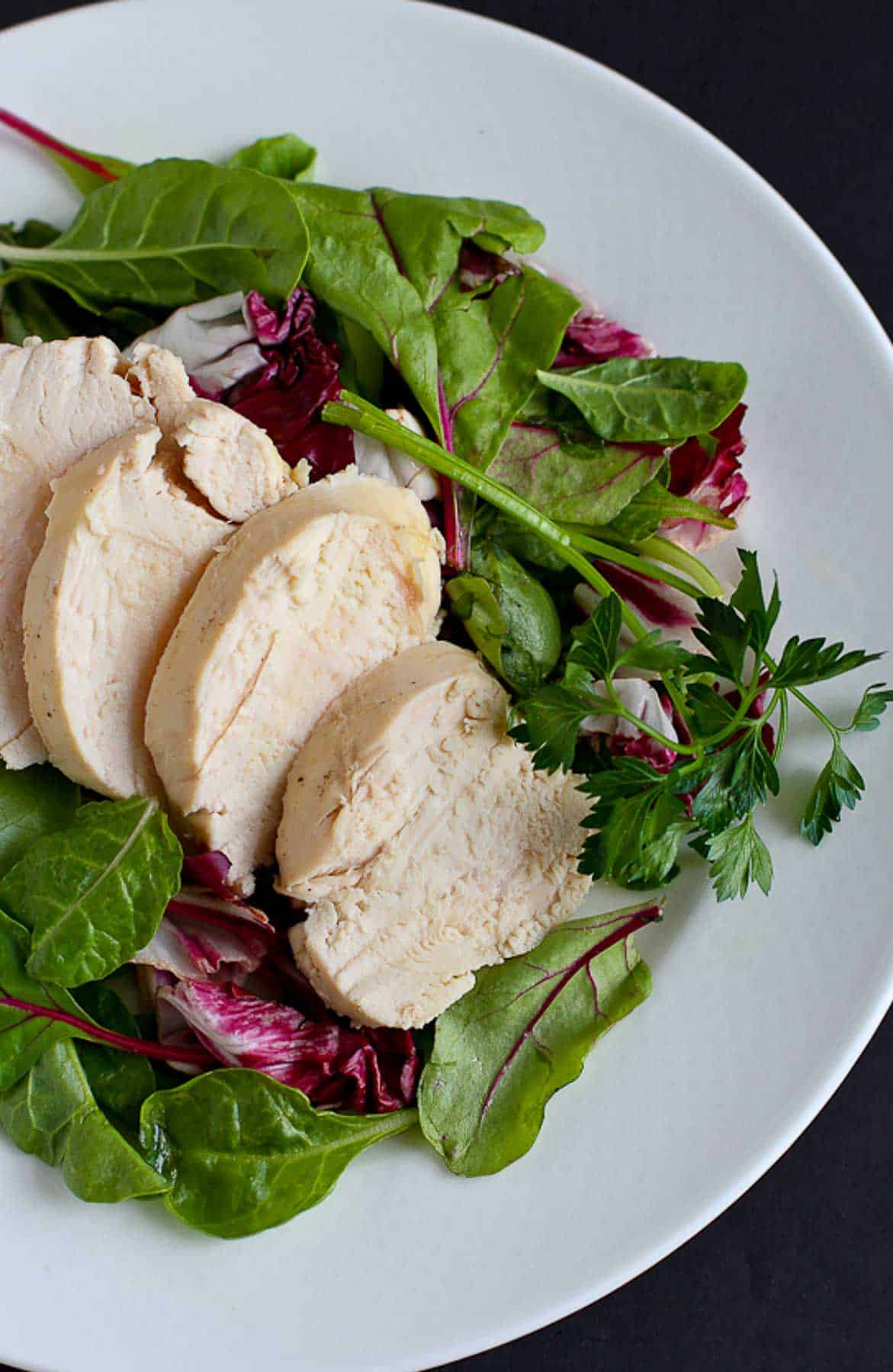 Salad with sliced chicken on a white plate.