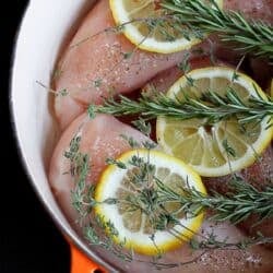 Lemon slices, rosemary sprigs and raw chicken in a pan.