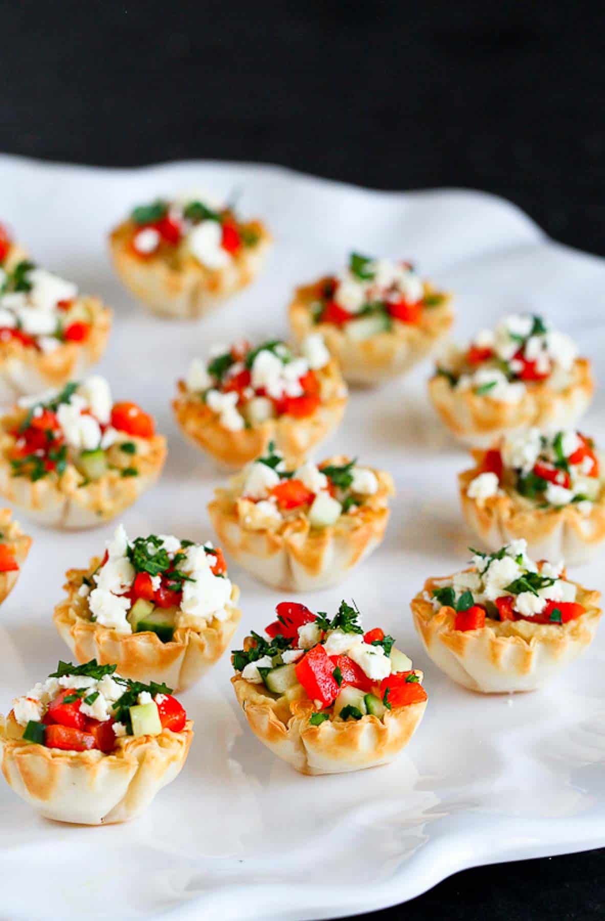 Mini phyllo cups filled with vegetable and feta, all on a white platter.