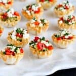 Mini phyllo cups filled with vegetable and feta, all on a white platter.
