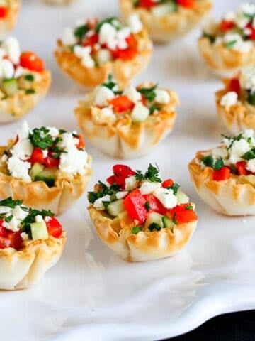 Mini phyllo cups filled with vegetable and feta, all on a white platter.