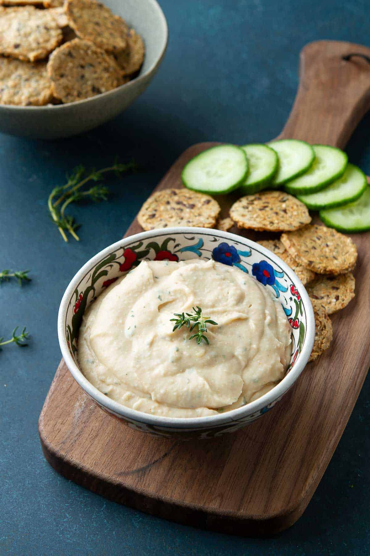 Cannellini bean dip in a bowl, crackers and cucumber on a wood serving board.