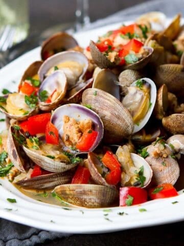 Steamed clams, sausage and red pepper in a white bowl.