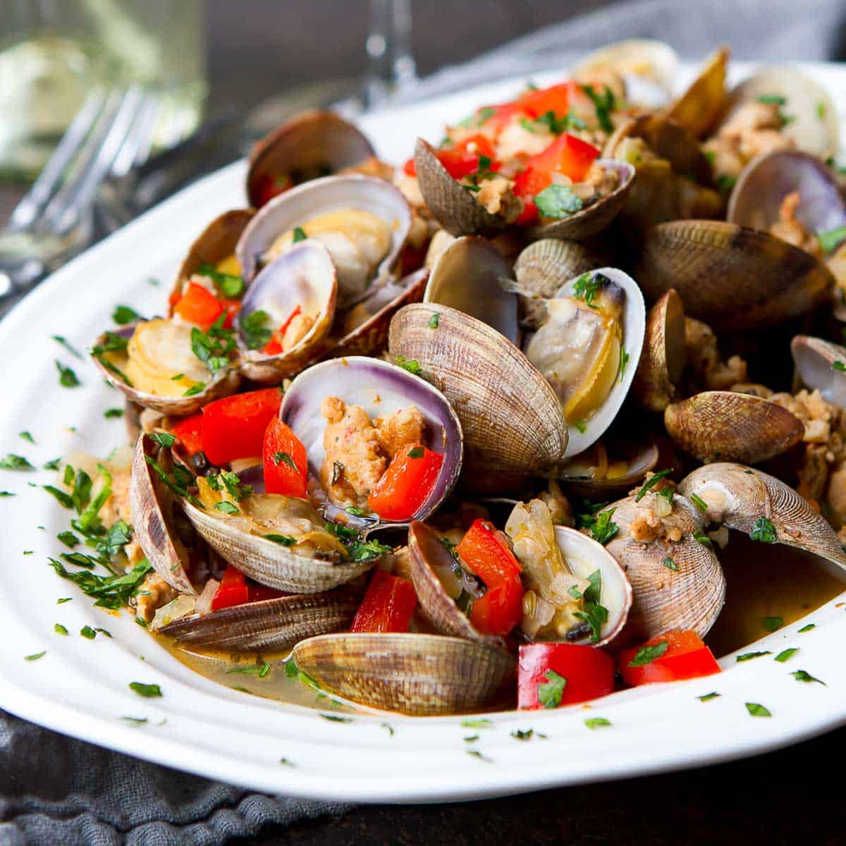 Steamed clams, sausage and red pepper in a white bowl.