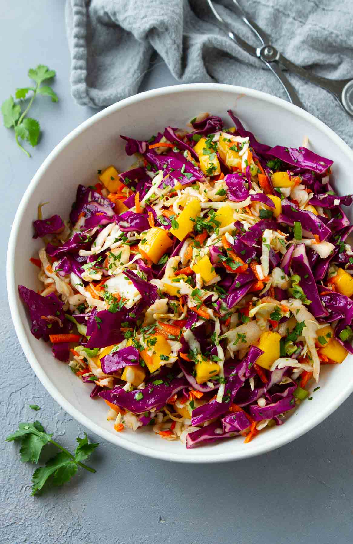 Green and purple cabbage slaw with mango in a glass bowl.
