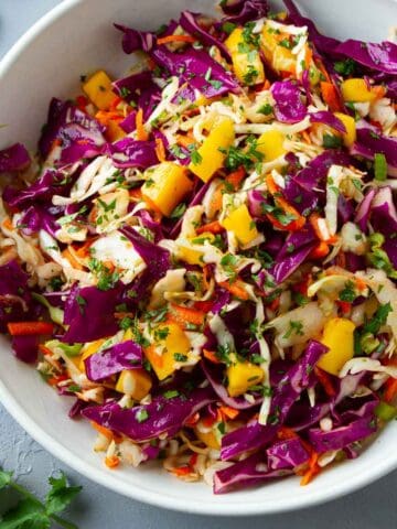 Green and purple cabbage slaw with mango in a white bowl.