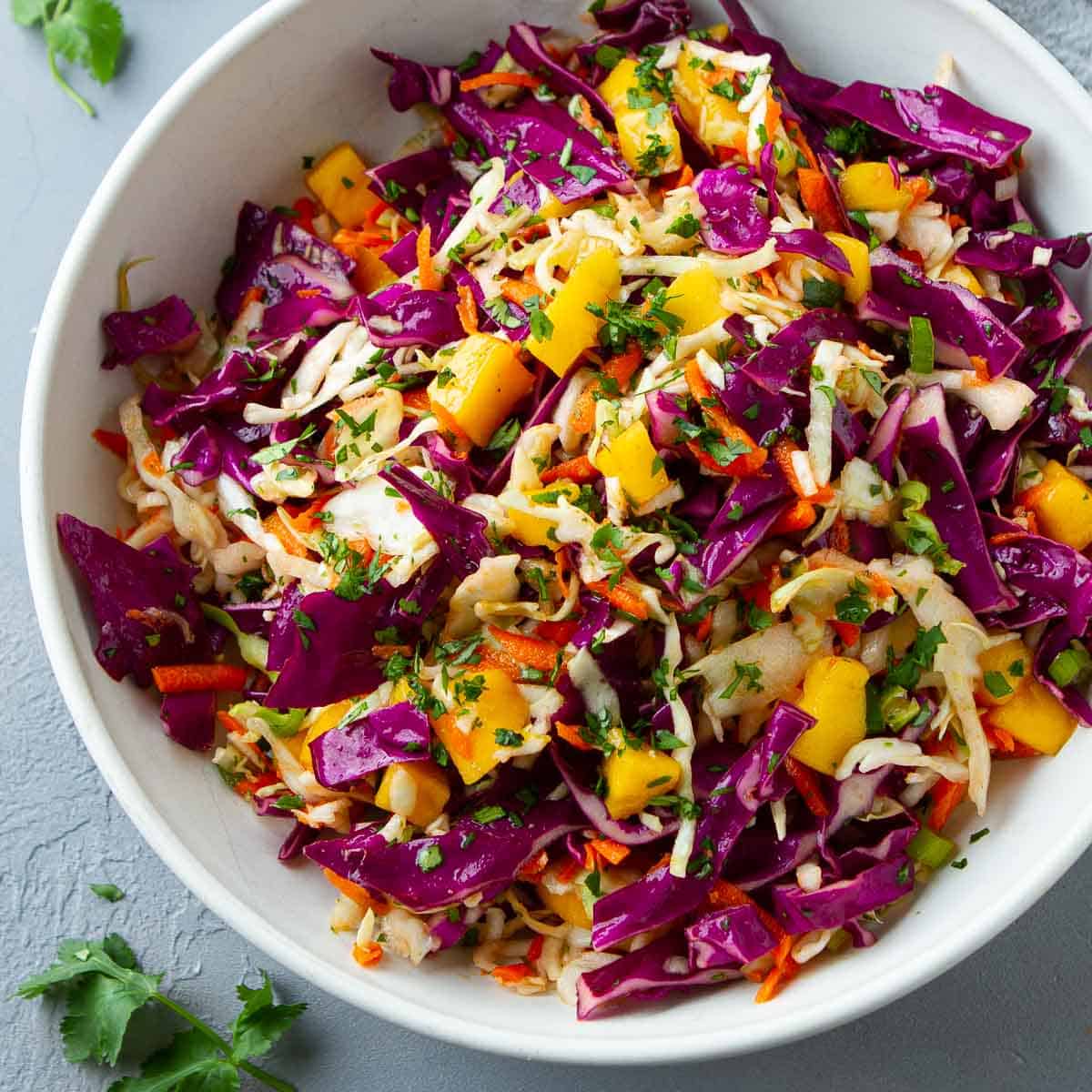 Green and purple cabbage slaw with mango in a white bowl.