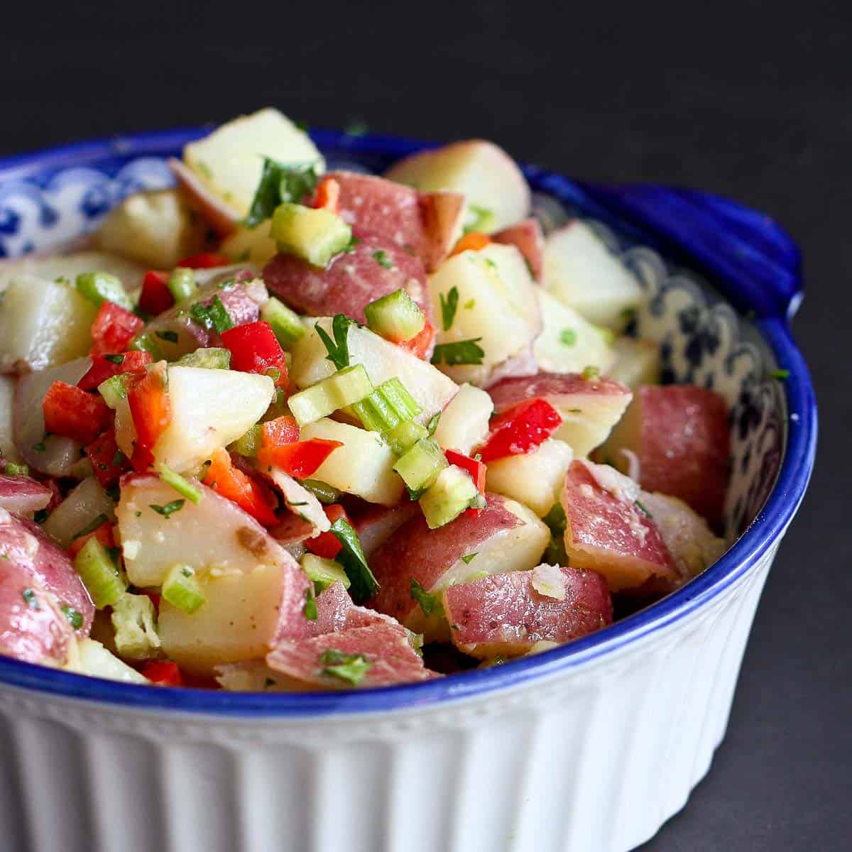 Potato salad with red pepper and celery in a blue and white bowl.