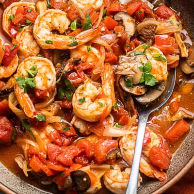Shrimp, tomato and mushroom stew in a brown bowl.