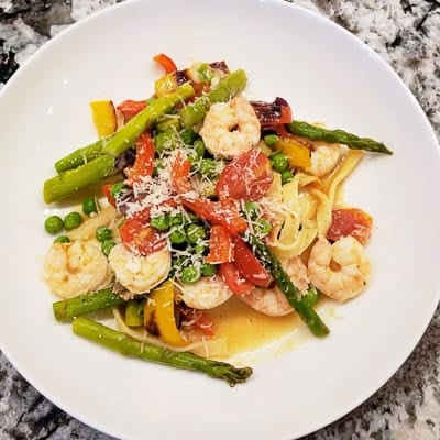 Shrimp, pasta and vegetables in a white bowl.