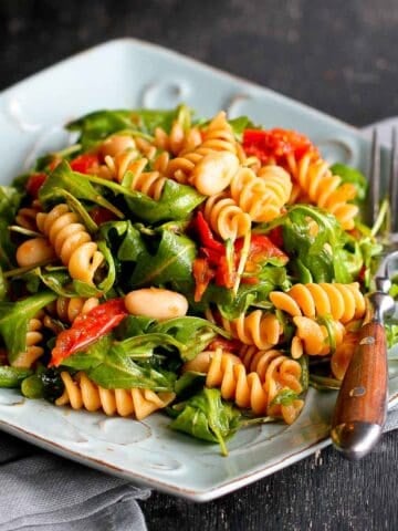 Pasta salad with arugula, beans and tomatoes on a light blue plate.