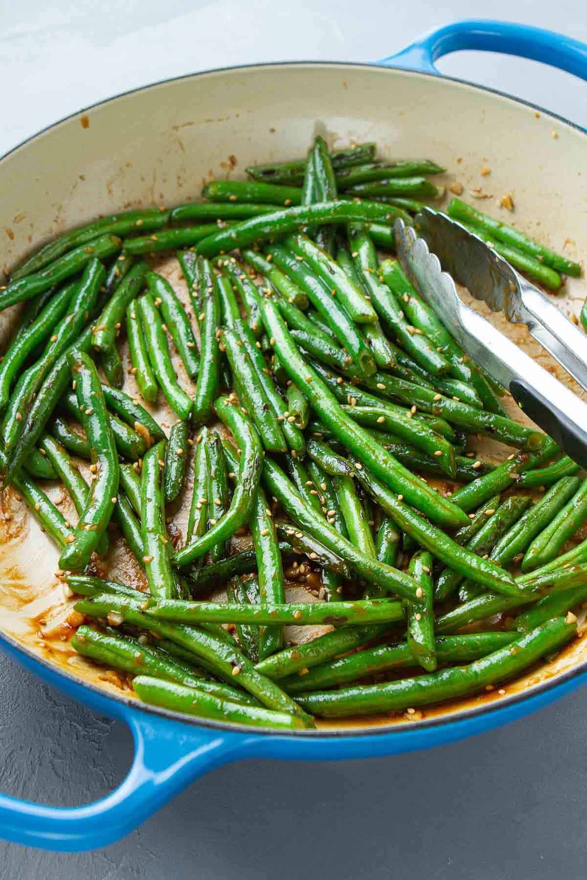Stir-fried green beans and tongs in a large ceramic skillet.