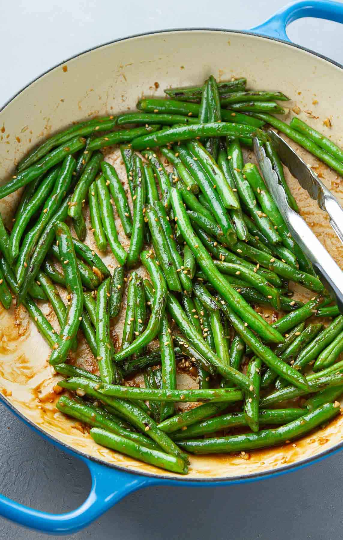 Glazed green beans in a large ceramic skillet, with tongs.