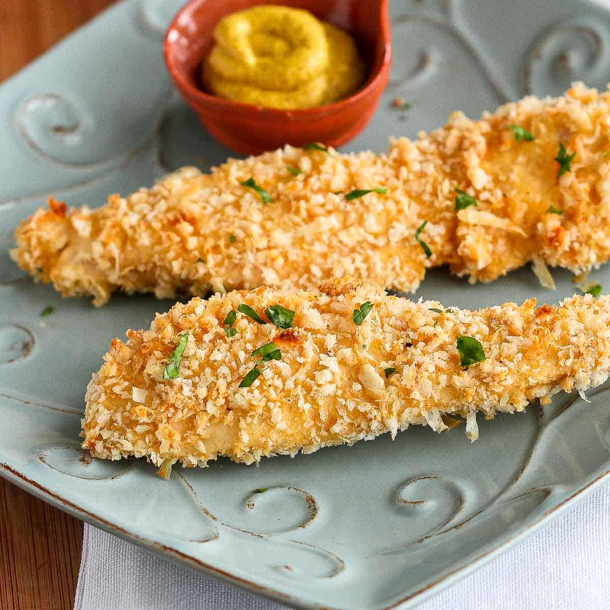 Crusted chicken strips on a blue plate with a side of mustard.