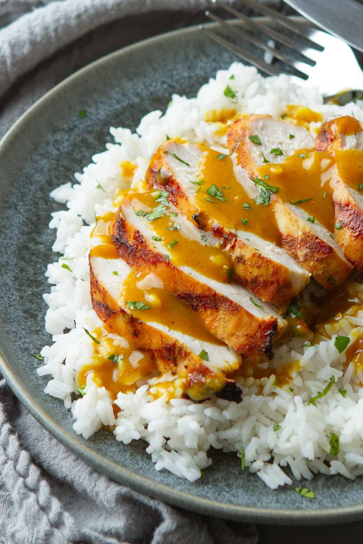 Sliced chicken breast on a bed of rice, drizzled with a curry sauce.