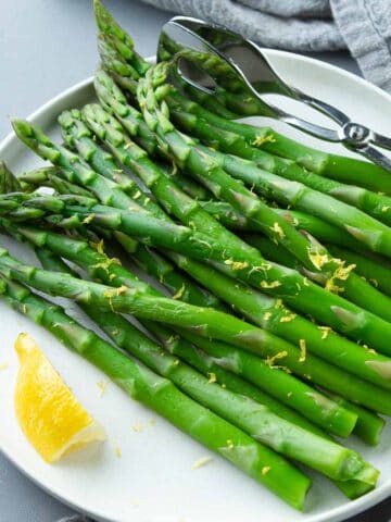Cooked asparagus and lemon wedge on a white plate.