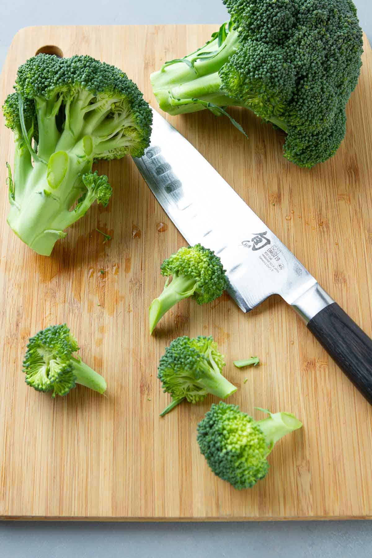 Broccoli crown, florets and a knife on a cutting board.