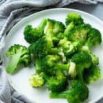 Steamed broccoli florets on a white plate.