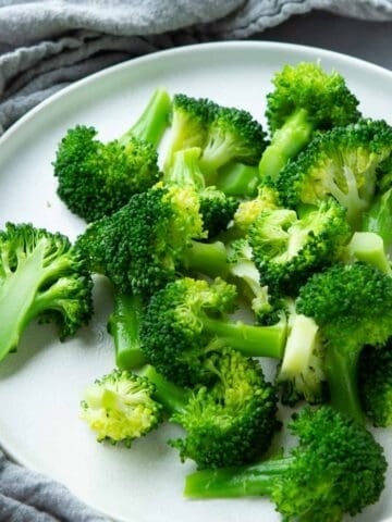 Steamed broccoli florets on a white plate.