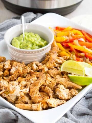 Cooked chicken, peppers and guacamole on a white platter.