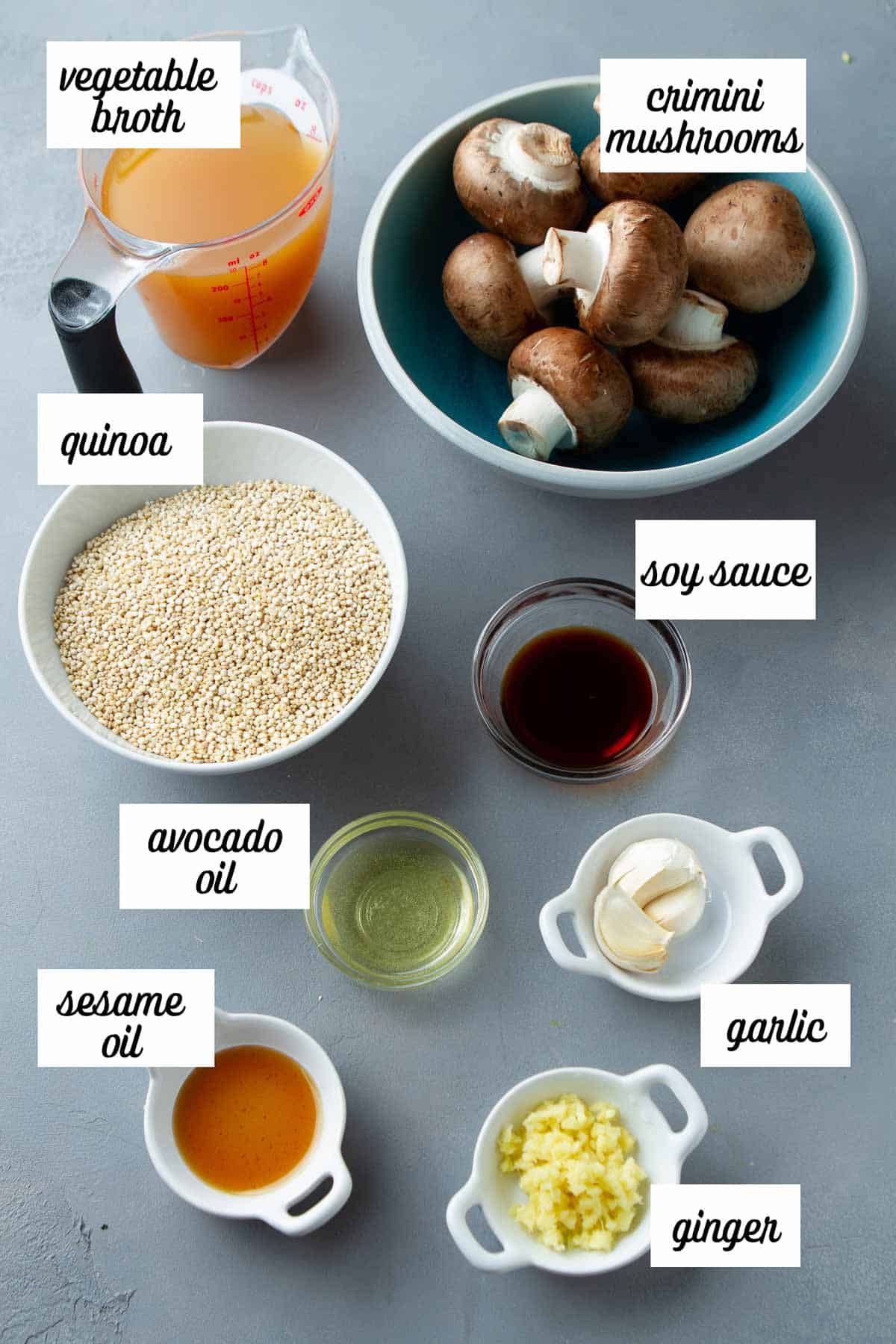 Labeled ingredients for mushroom quinoa recipe on a gray background.