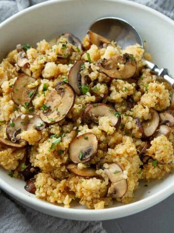 Mushrooms and quinoa in a white bowl with a spoon.