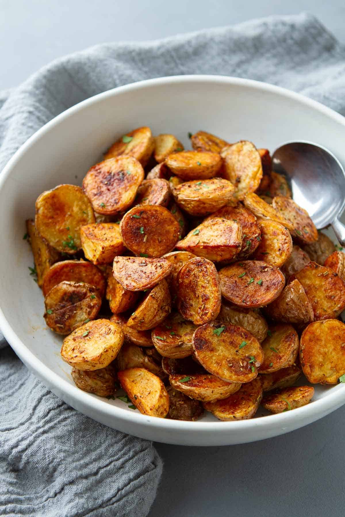 Roasted potatoes and a spoon in a white bowl.