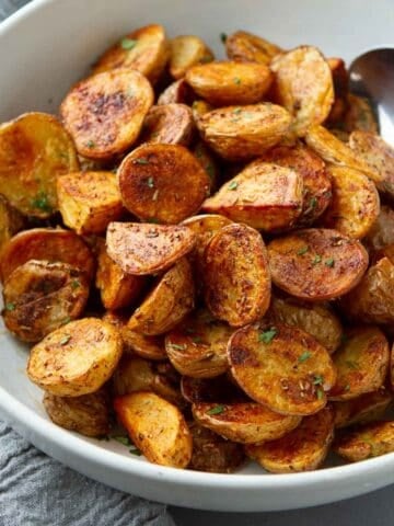 Spice-coated potatoes in a white bowl with a spoon.