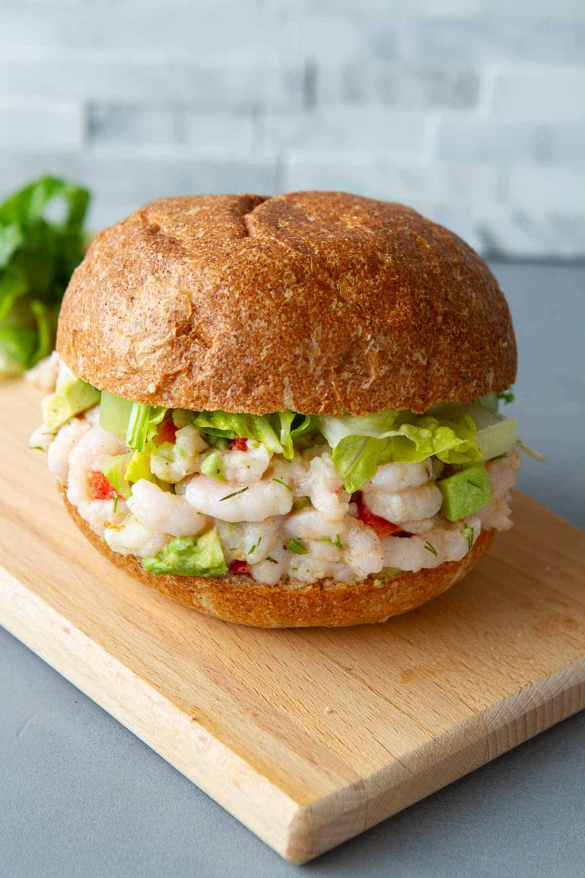 Shrimp avocado sandwich on a wheat roll, sitting on a cutting board.