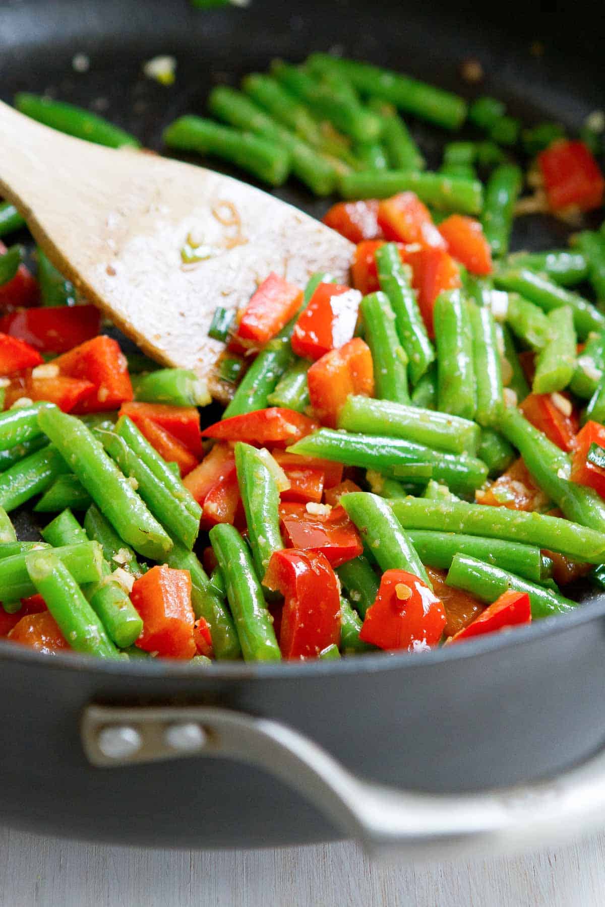 Green beans and red bell peppers being stir fried in a nonstick pan with garlic and ginger.