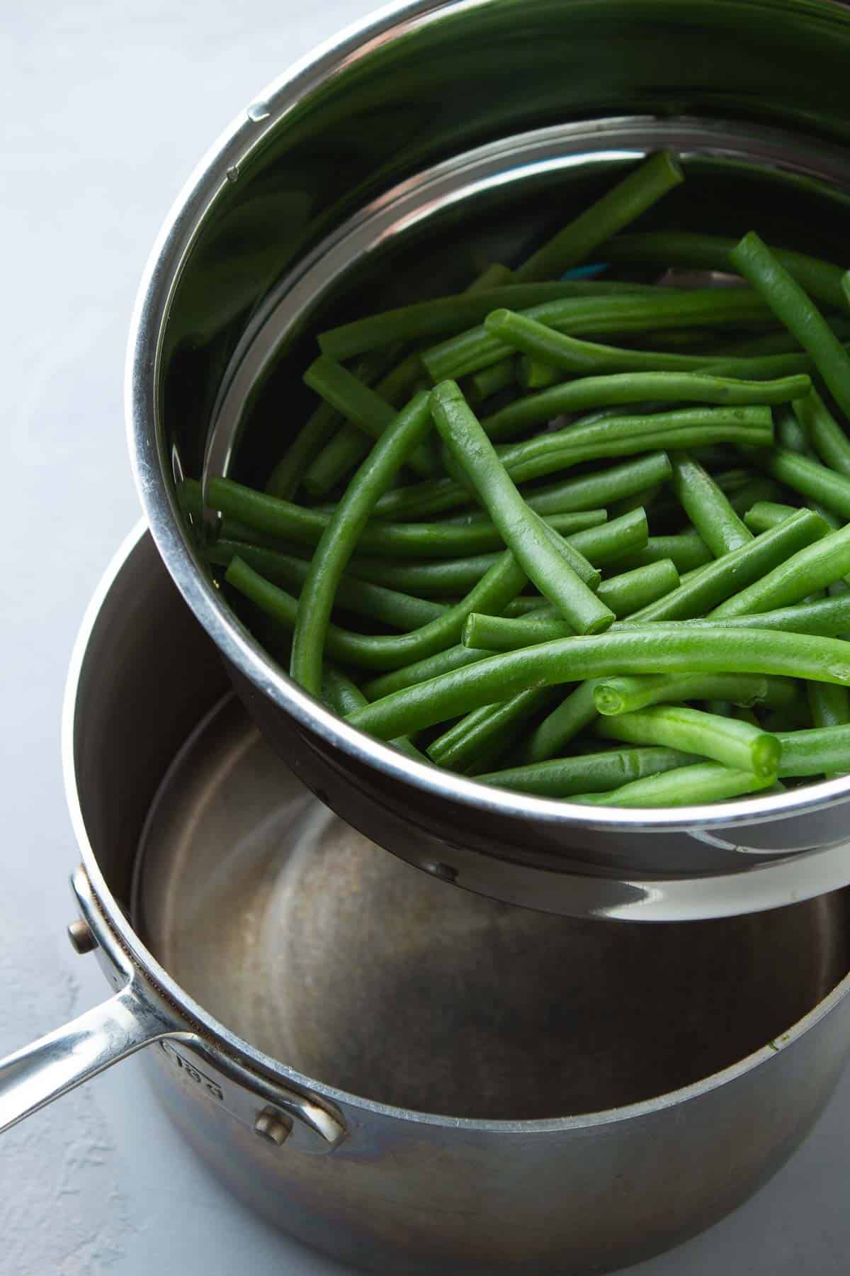 Steamer with green beans over a saucepan of water.