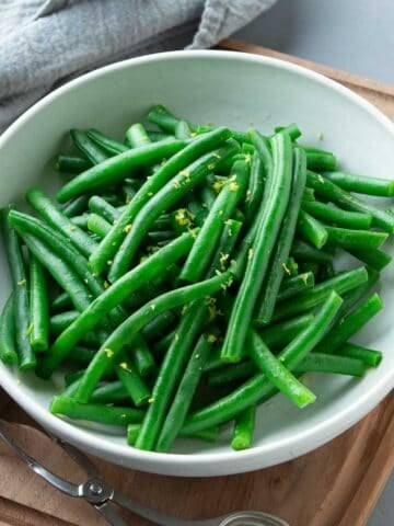 Steamed green beans with lemon zest in a white bowl.
